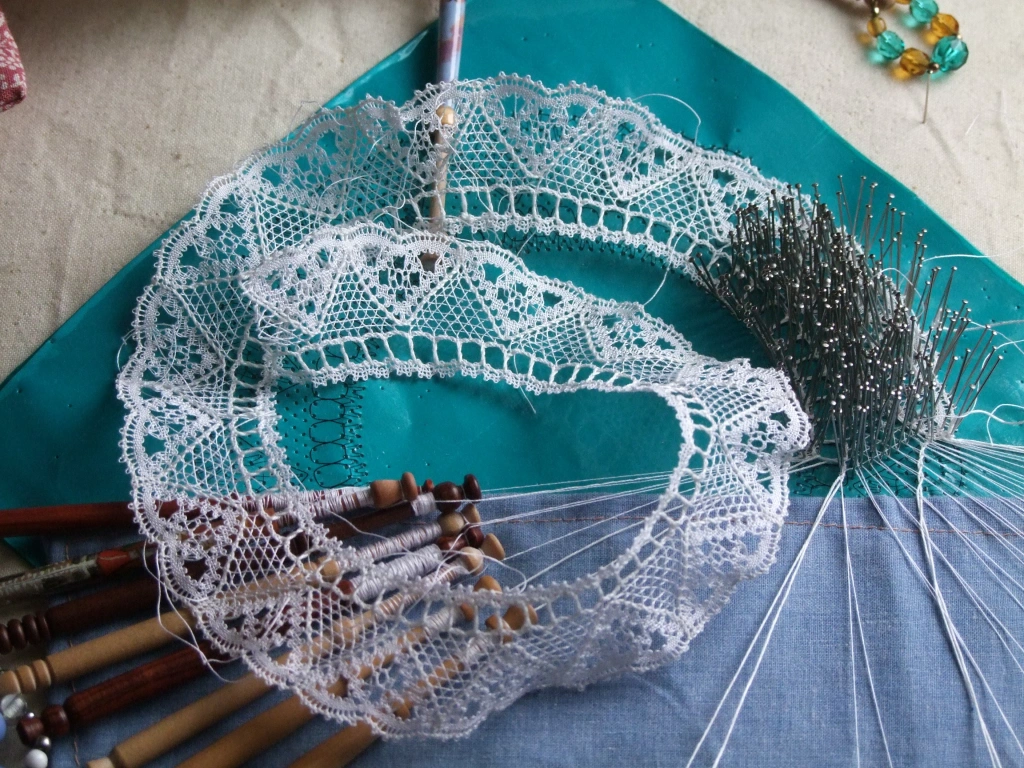 Bobbin lace collar on a pillow, with some bobbins still attached